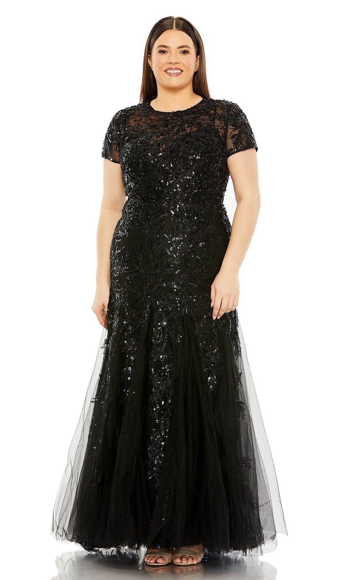 A woman models the Long Plus-Size Prom Dress 20623 by Mac Duggal—a floor-length black lace gown with short sleeves and sequin embellishments—standing against a white background.